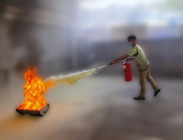 A trainee in a face mask uses a red fire extinguisher on a fire pit during a fire fighting training exercise.